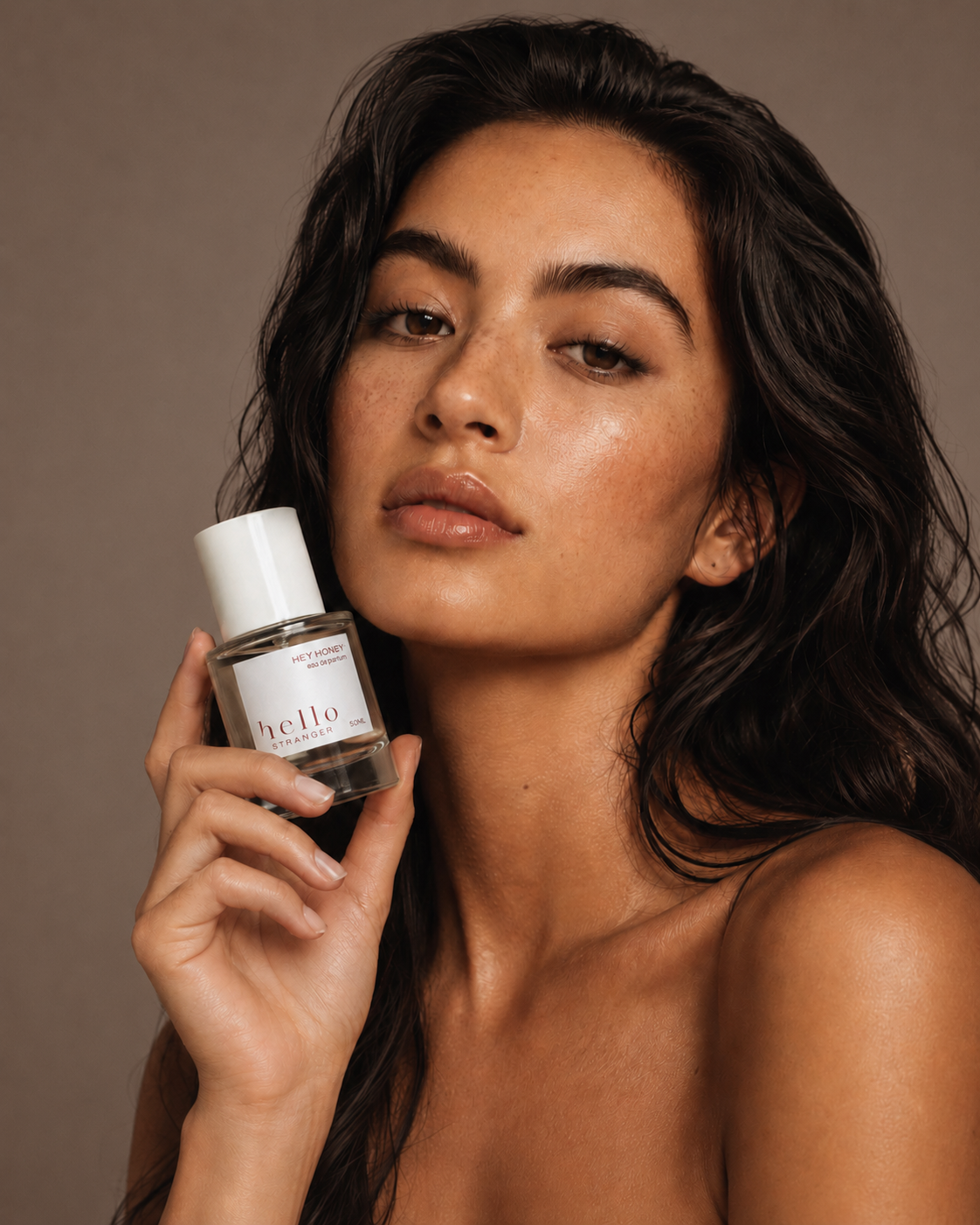 Woman holding a bottle of 'hello' perfume against a brown background